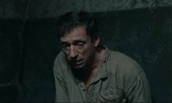 Movie still from “The Confession” (1970), directed by Costa-Gavras – A man in a brown shirt is sitting in a dark room; Close Up shot, High angle