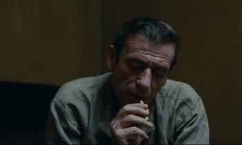 Movie still from “The Confession” (1970), directed by Costa-Gavras – A person sitting down with a cigarette in his mouth; Close Up shot, High angle