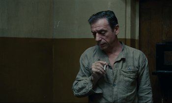 Movie still from “The Confession” (1970), directed by Costa-Gavras – A man standing in front of a wall holding a cell phone; Close Up shot, Over the shoulder angle