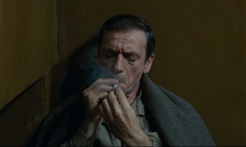 Movie still from “The Confession” (1970), directed by Costa-Gavras – A man smoking a cigarette while wrapped in a blanket; Close Up shot, High angle