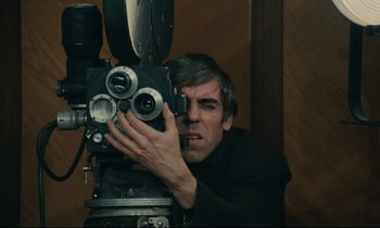 Movie still from “The Confession” (1970), directed by Costa-Gavras – A man is taking a picture with an old movie camera; Medium shot, Low angle