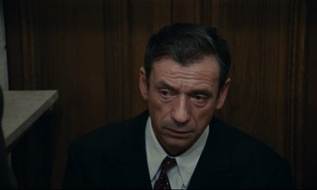 Movie still from “The Confession” (1970), directed by Costa-Gavras – A person wearing a suit and tie; Close Up shot, High angle