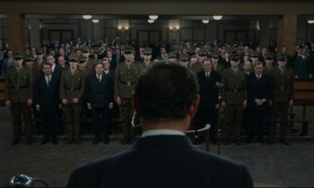 Movie still from “The Confession” (1970), directed by Costa-Gavras – A group of men standing in front of each other in a room; Wide shot, High angle