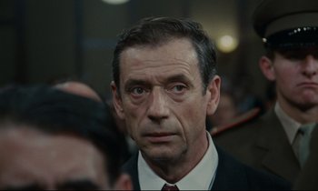 Movie still from “The Confession” (1970), directed by Costa-Gavras – A person wearing a suit and tie; Close Up shot, Low angle