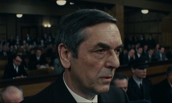 Movie still from “The Confession” (1970), directed by Costa-Gavras – A person wearing a suit and tie; Close Up shot, Over the shoulder angle