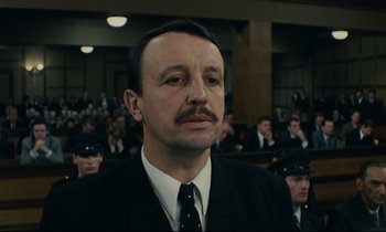Movie still from “The Confession” (1970), directed by Costa-Gavras – A man in a suit and tie in front of a group of people; Close Up shot, Low angle