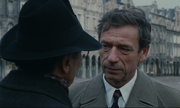 Movie still from “The Confession” (1970), directed by Costa-Gavras – A man wearing a hat and a suit talking to another man wearing a hat and a suit; Close Up shot, Over the shoulder angle
