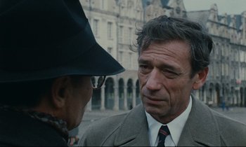 Movie still from “The Confession” (1970), directed by Costa-Gavras – A man in a suit talking to another man in a hat; Close Up shot, Over the shoulder angle