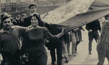 Movie still from “The Confession” (1970), directed by Costa-Gavras – A group of people walking down a street holding a flag; Medium shot, High angle