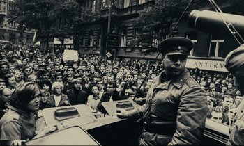 Movie still from “The Confession” (1970), directed by Costa-Gavras – A man in a military uniform stands in front of a crowd of people; Wide shot, High angle