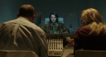 Movie still from “The Congress” (2013), directed by Ari Folman – A person sitting in front of a microphone in front of other people; Medium shot, Over the shoulder angle