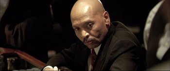 Movie still from “The Cooler” (2003), directed by Wayne Kramer – A bald man in a black suit and a red neck tie; Close Up shot, Low angle