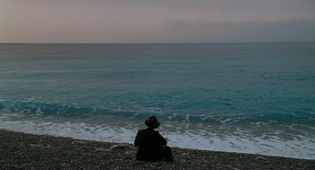 Movie still from “The Counterfeiters” (2007), directed by Stefan Ruzowitzky – A man sitting on the beach looking out at the ocean; Extreme Wide shot, High angle