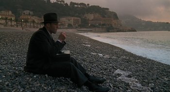 Movie still from “The Counterfeiters” (2007), directed by Stefan Ruzowitzky – A man sitting on the beach with a cigarette in his mouth; Wide shot, Low angle