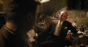 Movie still from “The Counterfeiters” (2007), directed by Stefan Ruzowitzky – A man sitting in a chair in front of another man in a suit; Medium shot, Over the shoulder angle