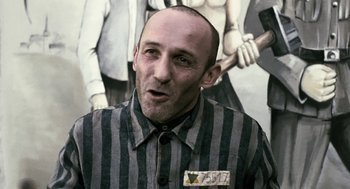Movie still from “The Counterfeiters” (2007), directed by Stefan Ruzowitzky – A man in a striped shirt is standing in front of a painting; Medium shot, Over the shoulder angle