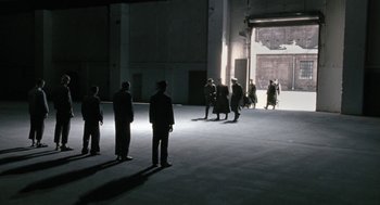 Movie still from “The Counterfeiters” (2007), directed by Stefan Ruzowitzky – A group of people standing in a dark room; Extreme Wide shot, High angle