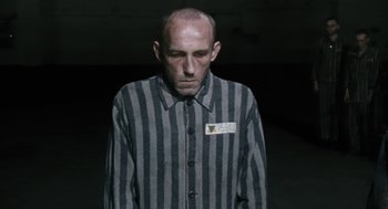Movie still from “The Counterfeiters” (2007), directed by Stefan Ruzowitzky – A man in a striped shirt is standing in a dark room; Medium shot, Over the shoulder angle
