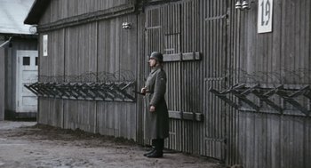Movie still from “The Counterfeiters” (2007), directed by Stefan Ruzowitzky – A man standing in front of a wooden building; Wide shot, High angle