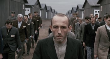 Movie still from “The Counterfeiters” (2007), directed by Stefan Ruzowitzky – A group of men in suits walking down a dirt road; Medium shot, Over the shoulder angle