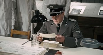 Movie still from “The Counterfeiters” (2007), directed by Stefan Ruzowitzky – A man in uniform sitting at a table reading a piece of paper; Medium shot, High angle