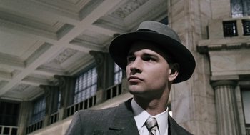 Movie still from “The Counterfeiters” (2007), directed by Stefan Ruzowitzky – A man wearing a suit and hat in front of a building; Close Up shot, Low angle