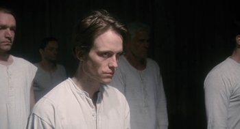 Movie still from “The Counterfeiters” (2007), directed by Stefan Ruzowitzky – A man in a white shirt is standing in front of two other men; Close Up shot, Low angle