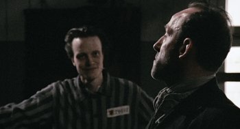 Movie still from “The Counterfeiters” (2007), directed by Stefan Ruzowitzky – A man in a prison uniform talking to another man in a prison uniform; Medium shot, Over the shoulder angle