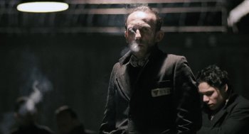 Movie still from “The Counterfeiters” (2007), directed by Stefan Ruzowitzky – A man in a black suit smoking a cigarette; Close Up shot, Over the shoulder angle