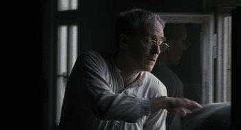 Movie still from “The Counterfeiters” (2007), directed by Stefan Ruzowitzky – An older man wearing glasses is looking out a window; Close Up shot, Over the shoulder angle