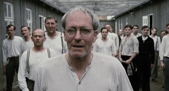 Movie still from “The Counterfeiters” (2007), directed by Stefan Ruzowitzky – An old man with glasses standing in front of a group of men; Close Up shot, Low angle