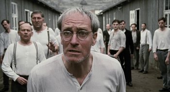 Movie still from “The Counterfeiters” (2007), directed by Stefan Ruzowitzky – An older man in a white shirt is in a crowd of people; Close Up shot, Over the shoulder angle