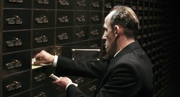 Movie still from “The Counterfeiters” (2007), directed by Stefan Ruzowitzky – A man in a black suit and white shirt is putting a card in a card catalog; Close Up shot, Low angle