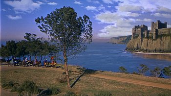 Movie still from “The Court Jester” (1955), directed by Melvin Frank – A group of people riding horses next to a body of water; Extreme Wide shot, High angle