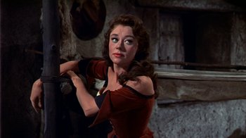 Movie still from “The Court Jester” (1955), directed by Melvin Frank – A beautiful woman in a red dress standing next to a pole; Medium shot, Low angle