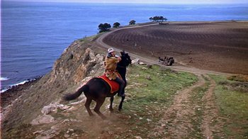 Movie still from “The Court Jester” (1955), directed by Melvin Frank – A man riding a horse down a hill next to the ocean; Extreme Wide shot, High angle