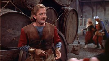 Movie still from “The Court Jester” (1955), directed by Melvin Frank – A man wearing a brown and red shirt standing in front of a bunch of wooden barrels; Medium shot, Over the shoulder angle