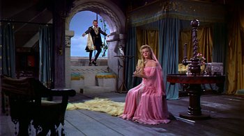 Movie still from “The Court Jester” (1955), directed by Melvin Frank – A woman in a pink dress sitting in front of a man in a black suit; Wide shot, High angle