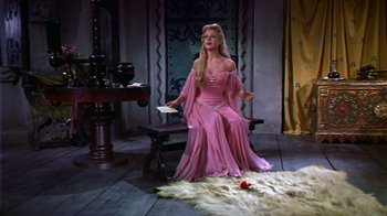 Movie still from “The Court Jester” (1955), directed by Melvin Frank – A woman in a pink dress sitting on a bench; Wide shot, High angle