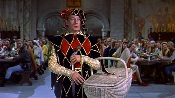 Movie still from “The Court Jester” (1955), directed by Melvin Frank – A man dressed as a medieval knight holding a basket; Wide shot, High angle