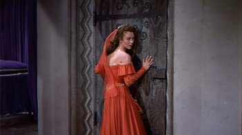 Movie still from “The Court Jester” (1955), directed by Melvin Frank – A woman in a red dress standing in front of a door; Medium shot, High angle