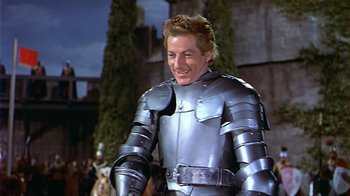 Movie still from “The Court Jester” (1955), directed by Melvin Frank – A man wearing a suit of armor smiles for the camera; Medium shot, Over the shoulder angle