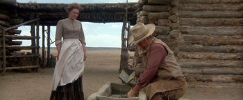 Movie still from “The Cowboys” (1972), directed by Mark Rydell – An older man and woman in a western setting; Wide shot, Low angle