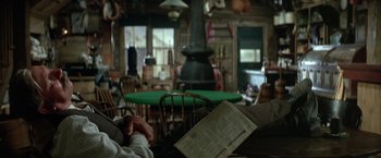 Movie still from “The Cowboys” (1972), directed by Mark Rydell – A person sitting at a table in front of a green table; Medium shot, High angle