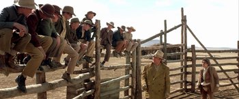 Movie still from “The Cowboys” (1972), directed by Mark Rydell – A group of men sitting on top of a wooden fence; Wide shot, Low angle