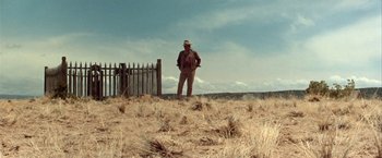 Movie still from “The Cowboys” (1972), directed by Mark Rydell – A man standing in a field with a fence behind him; Wide shot, Low angle