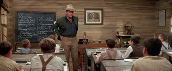 Movie still from “The Cowboys” (1972), directed by Mark Rydell – A man in a hat standing in front of a group of people; Medium shot, Over the shoulder angle