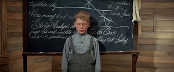 Movie still from “The Cowboys” (1972), directed by Mark Rydell – A young boy standing in front of a chalkboard; Medium shot, High angle