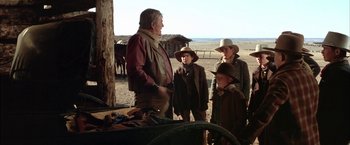 Movie still from “The Cowboys” (1972), directed by Mark Rydell – A group of people standing next to each other on a dirt field; Medium shot, Over the shoulder angle