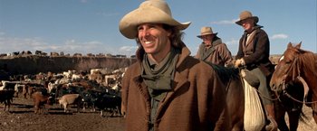 Movie still from “The Cowboys” (1972), directed by Mark Rydell – A man wearing a cowboy hat standing next to cows; Medium shot, Over the shoulder angle